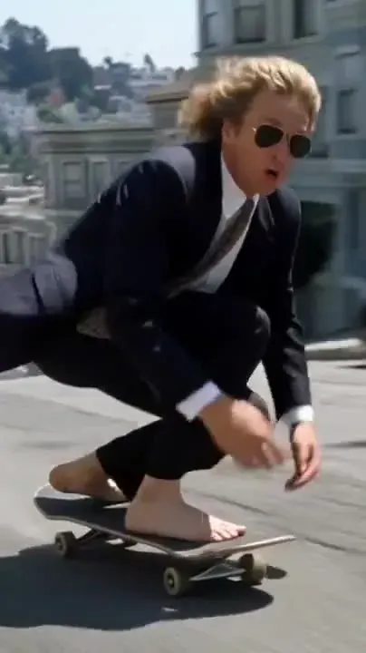 Grok imagine video prompt illustration: a man in a suit and aviators skateboarding barefoot down a steep city street, vertical frame