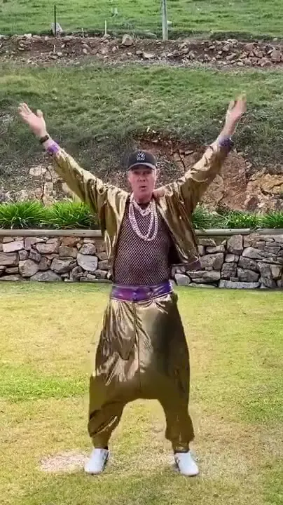 Motion reference, pose 1: a man in a gold lamé outfit and cap dancing with his arms raised on a lawn